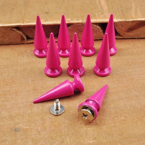 Peut inclure: Ensemble de clous roses vifs en forme de cône, avec un système de fixation à vis. Les clous sont disposés sur une surface en bois, certains debout et d'autres couchés, mettant en valeur leur design et leur système de fixation.