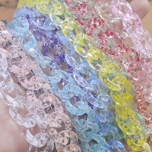May include: A close-up of a rainbow assortment of clear plastic chains with a speckled glitter finish. The chains are arranged in a fan shape, with the colors ranging from white to pink, blue, green, yellow, and red.