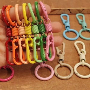 May include: A set of colorful metal keychains with spring loaded clips. The keychains are in various colors, including orange, yellow, green, blue, and pink.