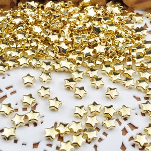 May include: A large pile of gold star-shaped beads. The beads are scattered on a white lace doily.