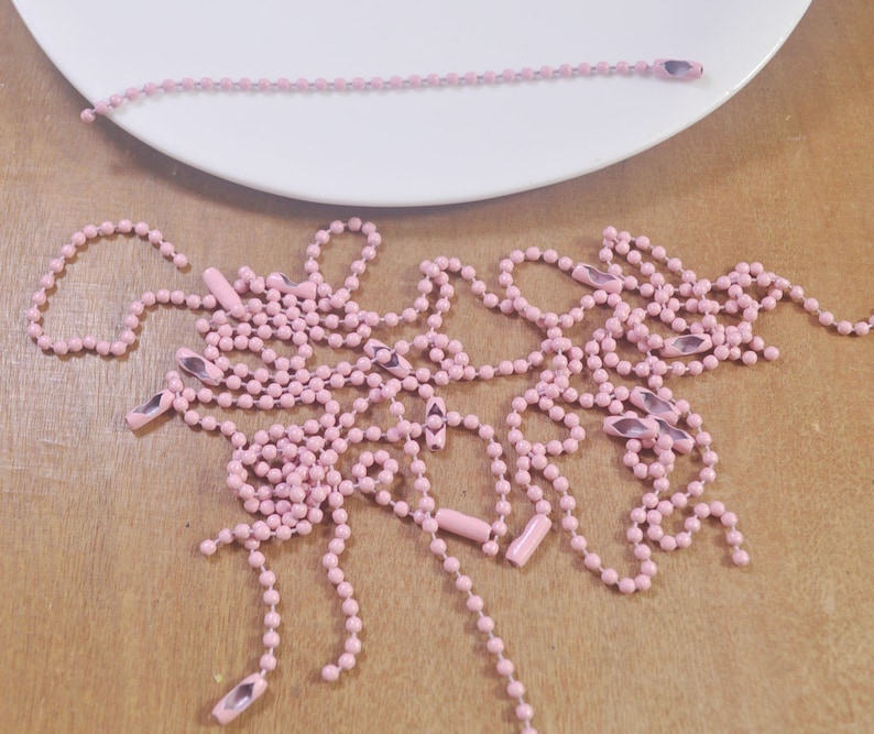 May include: A pile of pink metal chain with silver end caps. The chain is made of small, round links.
