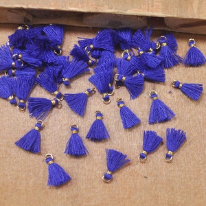 May include: A collection of small, blue tassels with gold accents. The tassels are scattered on a brown surface.
