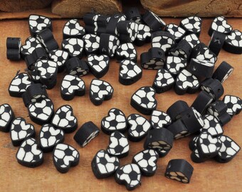Può includere: Una grande quantità di perline a forma di cuore nere e bianche con un design a pallone da calcio. Le perline sono realizzate in pasta polimerica e sono perfette per la creazione di gioielli o per l'artigianato.