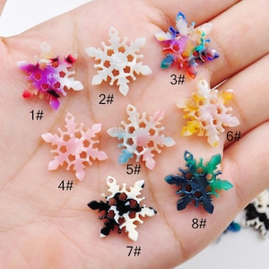 Könnte beinhalten: Acht Schneeflocken-Anhänger aus weißem, rosa, blauem, gelbem, grünem und schwarzem marmoriertem Kunststoff. Die Anhänger sind von 1 bis 8 nummeriert.