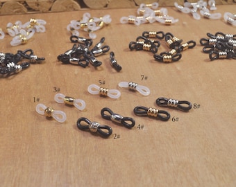 Puede incluir: Surtido de porta cadenas de gafas transparentes y negros con detalles dorados. Los porta cadenas están numerados del 1 al 8.
