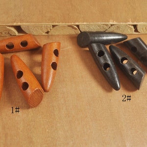 Könnte beinhalten: Zwei Sätze Holz-Toggle-Knöpfe. Der erste Satz ist braun und der zweite Satz ist schwarz. Beide Sätze haben zwei Löcher. Der braune Satz ist mit "1#" und der schwarze Satz mit "2#" gekennzeichnet.