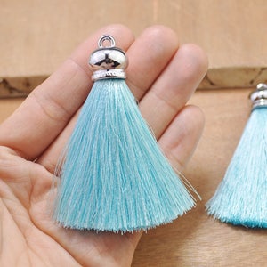 May include: Two light blue silk tassels with silver metal caps. The tassels are approximately 5 cm long.