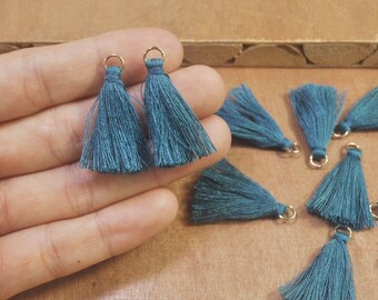 May include: Teal blue tassel trim with gold rings. The tassels are approximately 2 inches long.