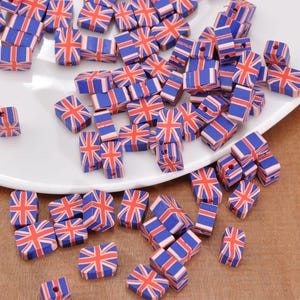 Pode incluir: Uma coleção de pequenas contas retangulares com o design da bandeira britânica Union Jack em vermelho, branco e azul. As contas estão espalhadas em um prato branco e em uma superfície de madeira.