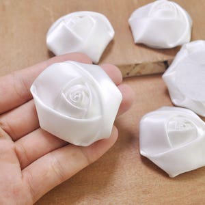 May include: Five white satin fabric rose flower embellishments. The roses are made of white satin ribbon and have a 3D effect.