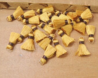 May include: A collection of gold tassel trim with brown accents and gold rings. The tassels are scattered on a wooden surface.