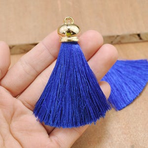 May include: A royal blue tassel with a gold metal top. The tassel is made of soft, silky threads and is approximately 2 inches long.