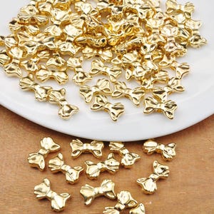 Puede incluir: Un montón grande de cuentas de metal de color dorado en forma de lazo. Las cuentas están esparcidas en un plato blanco.