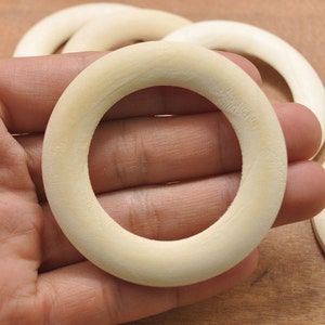 Puede incluir: Primer plano de un anillo de madera liso de color blanco roto. El anillo es grueso y tiene un gran diámetro interior.