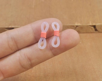 Puede incluir: Dos soportes para gafas de plástico blanco con una banda de goma naranja brillante alrededor del centro de cada soporte.