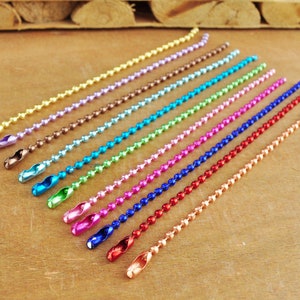 May include: Assortment of 14 colourful metal chain links with a beaded design. The chains are arranged in a row from lightest to darkest colour, starting with gold and ending with copper.