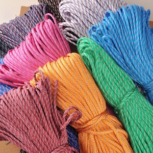 Könnte beinhalten: Eine Sammlung farbenfroher Seilbündel in verschiedenen Farbtönen, darunter Blau, Rosa, Orange, Grün und Burgunderrot. Jedes Bündel ist fest gewickelt und weist ein strukturiertes Muster auf. Die Seile scheinen aus einem strapazierfähigen Material zu bestehen.