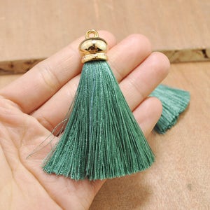 May include: A green tassel with a gold metal top. The tassel is made of soft, silky threads and is approximately 2 inches long.