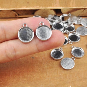 May include: Silver-toned metal pendant trays with a round shape and a smooth surface. The trays are designed for use with resin or other crafting materials.