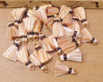 May include: A group of brown and white striped tassels with gold rings and brown trim. The tassels are arranged in a pile on a wooden surface.
