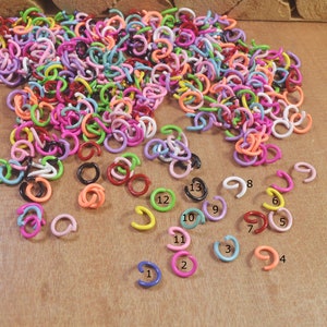 Puede incluir: Un montón grande de anillos de salto de metal de colores en varios tamaños. Los anillos están dispuestos en un montón sobre una superficie de madera. Hay 13 anillos individuales separados del montón, numerados del 1 al 13.