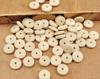 May include: A large pile of natural wood round beads with a hole in the center. The beads are light brown in color and are scattered on a wooden surface.