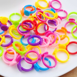 May include: A collection of colorful plastic rings with a flat, round base. The rings are in various colors, including red, orange, yellow, green, blue, purple, and pink.