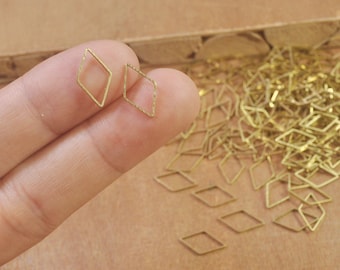May include: Two gold diamond-shaped metal rings, one held in a hand, with a pile of similar rings in the background.