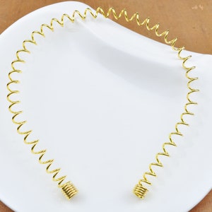 May include: A gold-coloured metal headband with a springy, coiled design. The headband is flexible and can be adjusted to fit different head sizes.