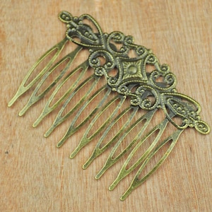 May include: A gold-toned metal hair comb with a decorative design featuring intricate swirls and a central diamond shape. The comb has nine teeth.