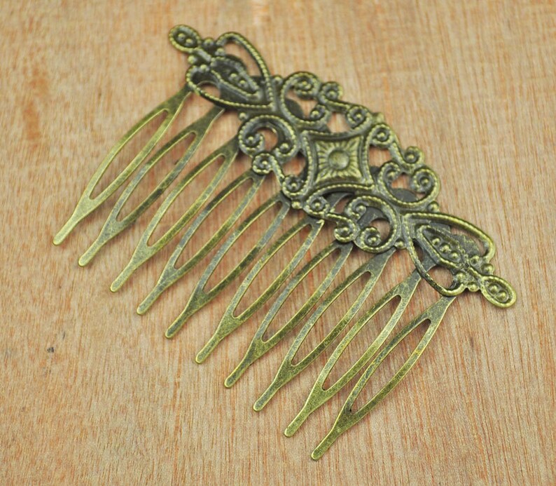 May include: A gold-toned metal hair comb with a decorative design featuring intricate swirls and a central diamond shape. The comb has nine teeth.
