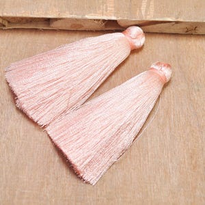 May include: Two pink silk tassels with a long, flowing fringe. The tassels are made of soft, delicate fabric and have a subtle sheen.