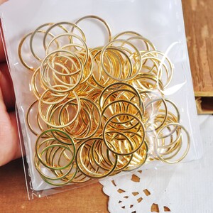 May include: A clear plastic bag filled with a large quantity of gold-colored metal jump rings. The rings are of various sizes and are arranged in a random pattern.