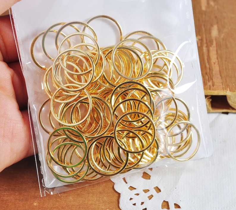 May include: A clear plastic bag filled with a large quantity of gold-colored metal jump rings. The rings are of various sizes and are arranged in a random pattern.