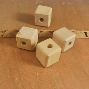 May include: Four unfinished wooden cubes with a hole in the centre of each. The cubes are arranged on a light brown surface.