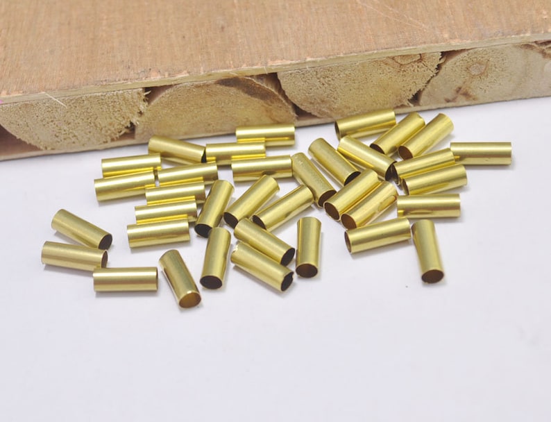 May include: A pile of gold-colored metal end caps for cords or wires. The end caps are cylindrical and have a smooth finish.