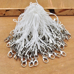 Op de afbeelding: Een grote stapel witte touwtjes met zilveren metalen karabijnhaken. De touwtjes zijn gebundeld en de karabijnhaken zijn verspreid rond de touwtjes.