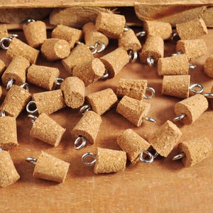 Può includere: Un gruppo di tappi per bottiglie di sughero marrone con anelli di metallo argentati. I tappi sono sparsi su una superficie di legno.