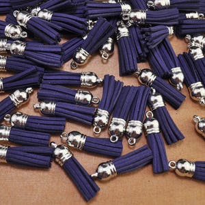 Peut inclure: Une collection de glands en daim violet avec des embouts en métal argenté. Les glands sont disposés sur une surface brune.