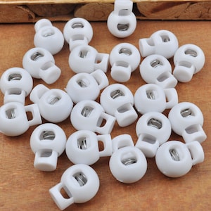 May include: A group of white plastic toggle clasps with a metal spring inside. The clasps are round and have a small hole on the side.