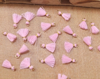 May include: A collection of pink tassel charms with gold jump rings. The tassels are made of soft yarn and are approximately 1 inch in length.