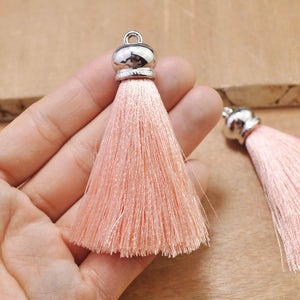May include: Two pink silk tassels with silver metal tops. The tassels are approximately 5 cm long and are held in a hand.