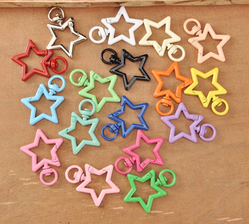 May include: A selection of star-shaped swivel clasps in a range of colours: red, silver, white, black, orange, yellow, green, blue, pink, and purple. These clasps are suitable for keychains, jewellery, or other craft projects.
