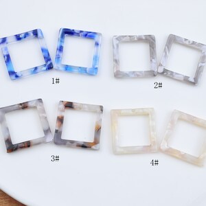 Könnte beinhalten: Vier Paare quadratischer Kunststoffrahmen mit verschiedenen Mustern. Die Rahmen sind weiß, grau, blau und braun. Die Rahmen sind von 1 bis 4 nummeriert.