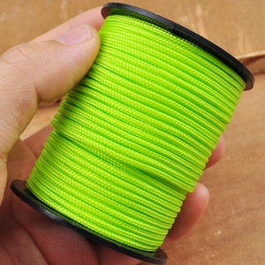 May include: A spool of bright green paracord, wound tightly around a black plastic spool.