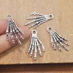 May include: Four silver skeleton hand charms with detailed bone structure. These charms are perfect for adding a spooky touch to jewelry or crafts.