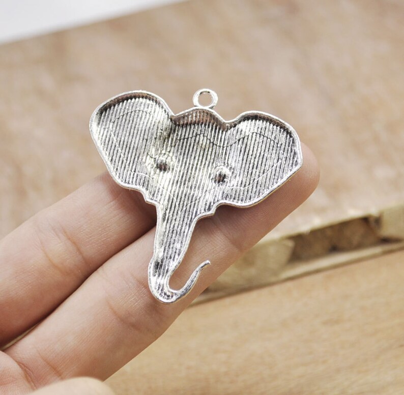 May include: Silver-toned metal elephant charm pendant with a textured surface. The charm has a loop at the top for attaching to a necklace or bracelet.