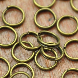 Puede incluir: Primer plano de un montón de pequeños anillos de salto de metal de color dorado. Los anillos son todos del mismo tamaño y están dispuestos en un patrón aleatorio.
