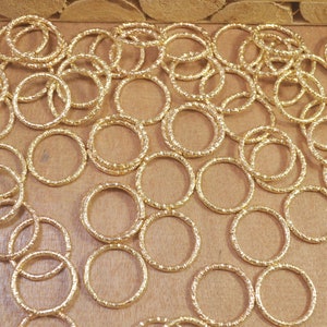 Puede incluir: Un gran grupo de anillos de metal de color dorado, todos del mismo tamaño y forma, están esparcidos sobre una superficie de madera. Los anillos son texturizados y tienen un acabado ligeramente rugoso.