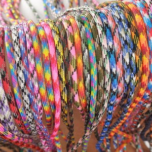 May include: A collection of colorful paracord lanyards in various patterns. The lanyards display a range of colors, including pink, blue, yellow, and green. The cords are tightly woven, creating a textured appearance. The image showcases a variety of designs.